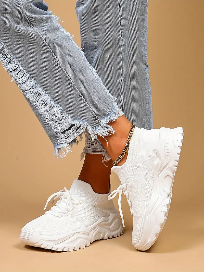 All-white knit sock sneakers with chunky soles, worn with ripped light-wash jeans.