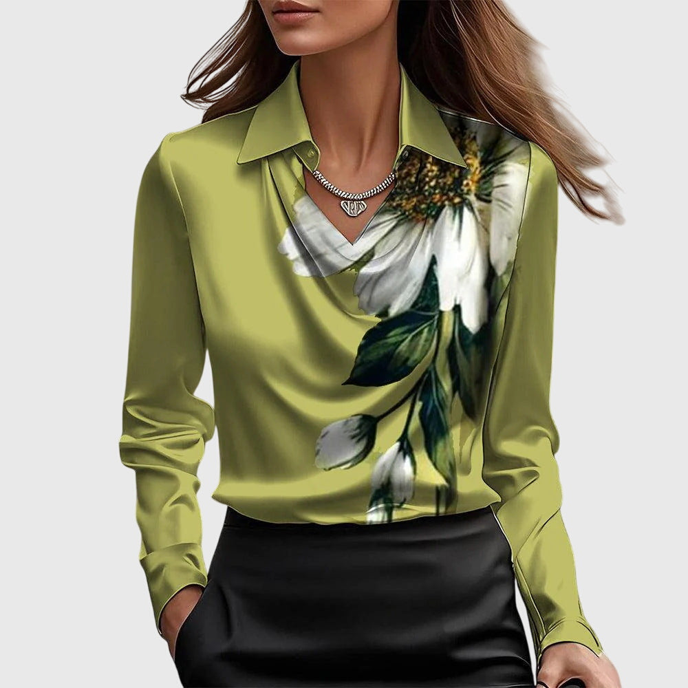 Model wearing the olive green satin blouse with a large white flower and green leaves printed down one side, with a draped cowl neckline.