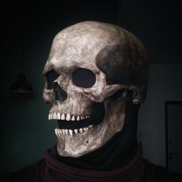 Skull mask worn by a person in a dark room, detail from the left with the lower jaw open wide.