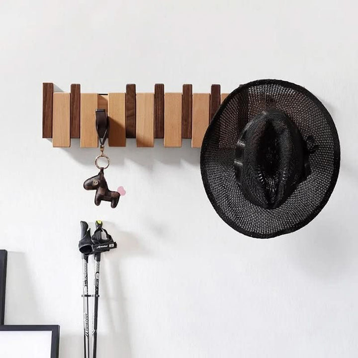 Brown wooden wall coat rack detail with a keychain on one hook and a black woven hat on the right.