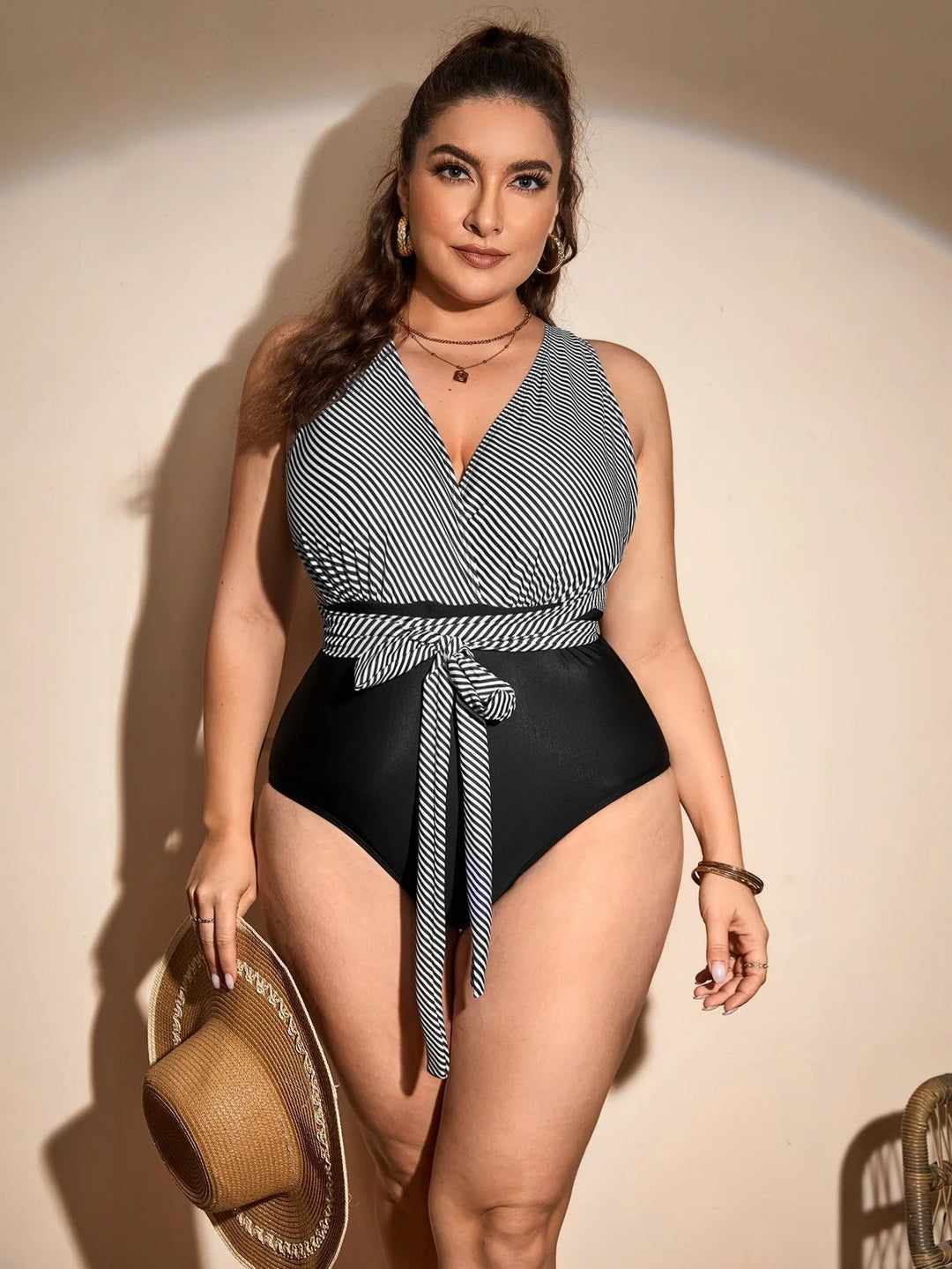 Frau im gestreiften Badeanzug mit Gürtel, hält Strohhut, Plus-Size-Mode, Sommerkleidung.