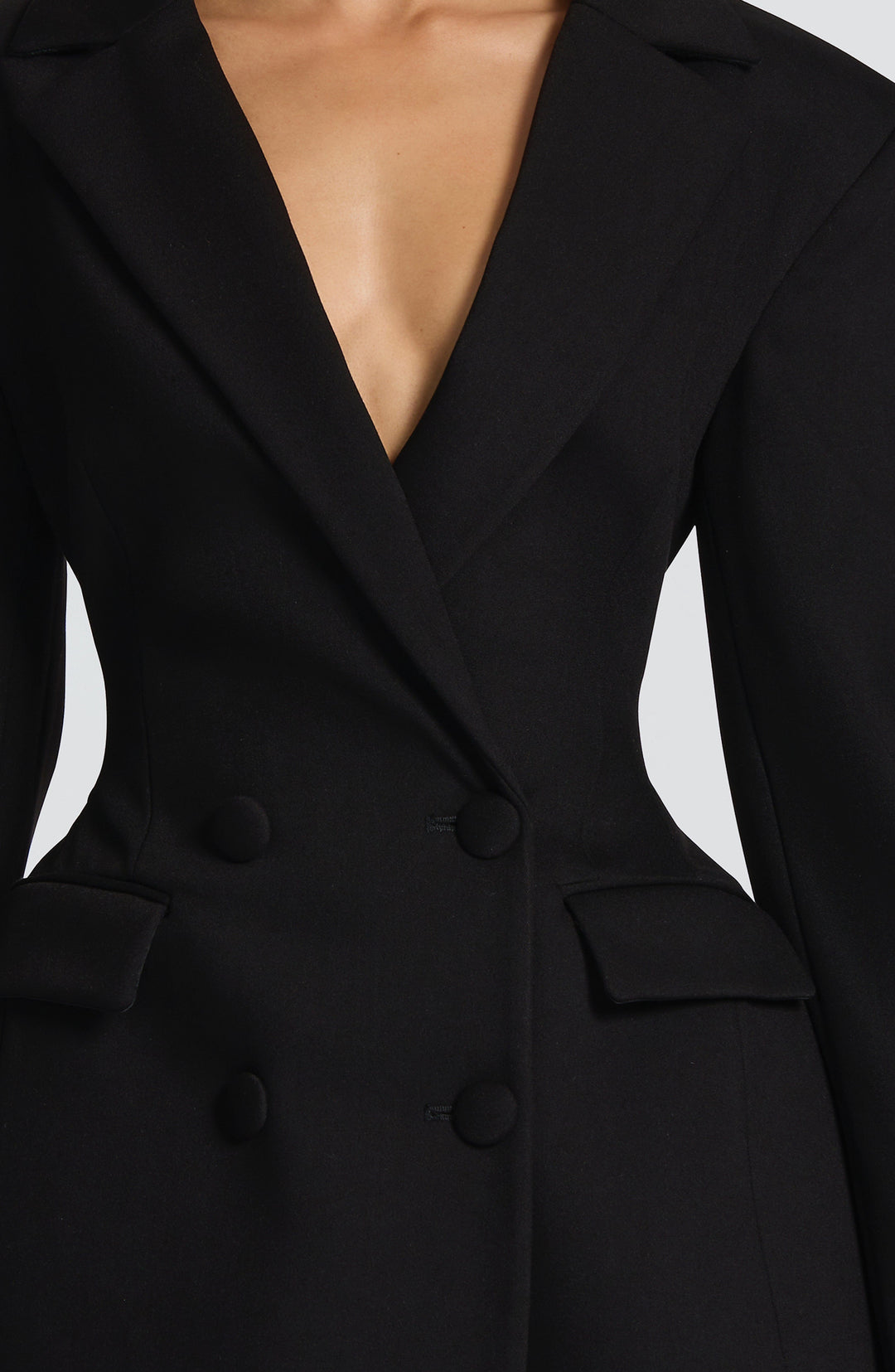 Black blazer mini dress bodice with a deep V neckline, notch lapels and flap pockets, detail.