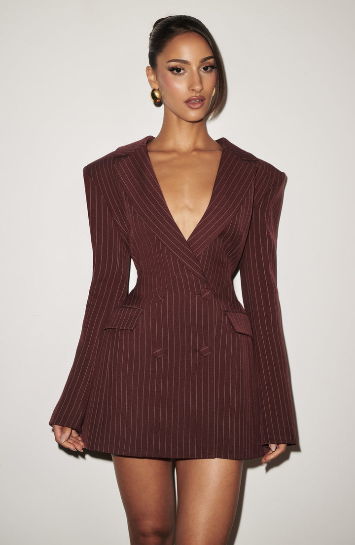 Close front view of a burgundy pinstripe double-breasted blazer dress with deep plunging lapels, structured shoulders and flap pockets, styled with gold earring 21