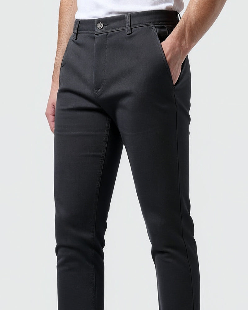Close-up of charcoal chinos at the waist and hip, showing the button, fly, belt loops and a hand resting in the side pocket. 10