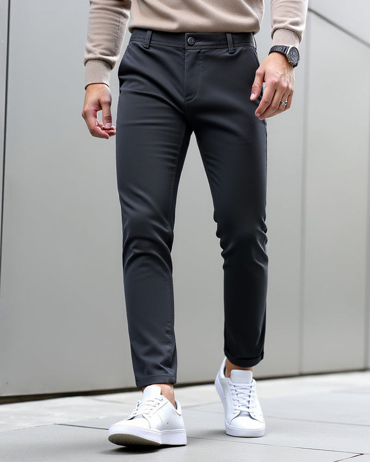 Charcoal chinos with cuffed hems styled with a beige knit sweater, black watch and white sneakers against a gray panel wall. 9
