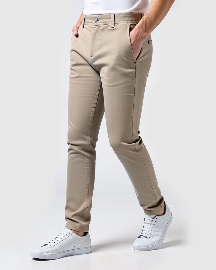 Beige khaki slim chinos in a three-quarter view with hands in the pockets, worn with a white tee and white sneakers. 14
