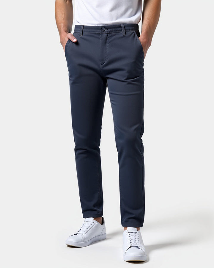 Front view of navy blue slim chinos worn with a white tee and white sneakers, both hands in the front pockets. 15