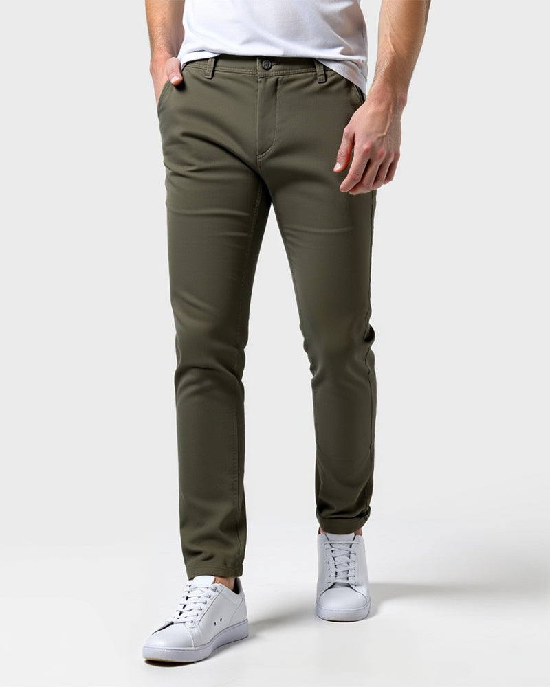 Front view of olive green slim chinos worn with a white tee and white sneakers, one hand in the front pocket. 13