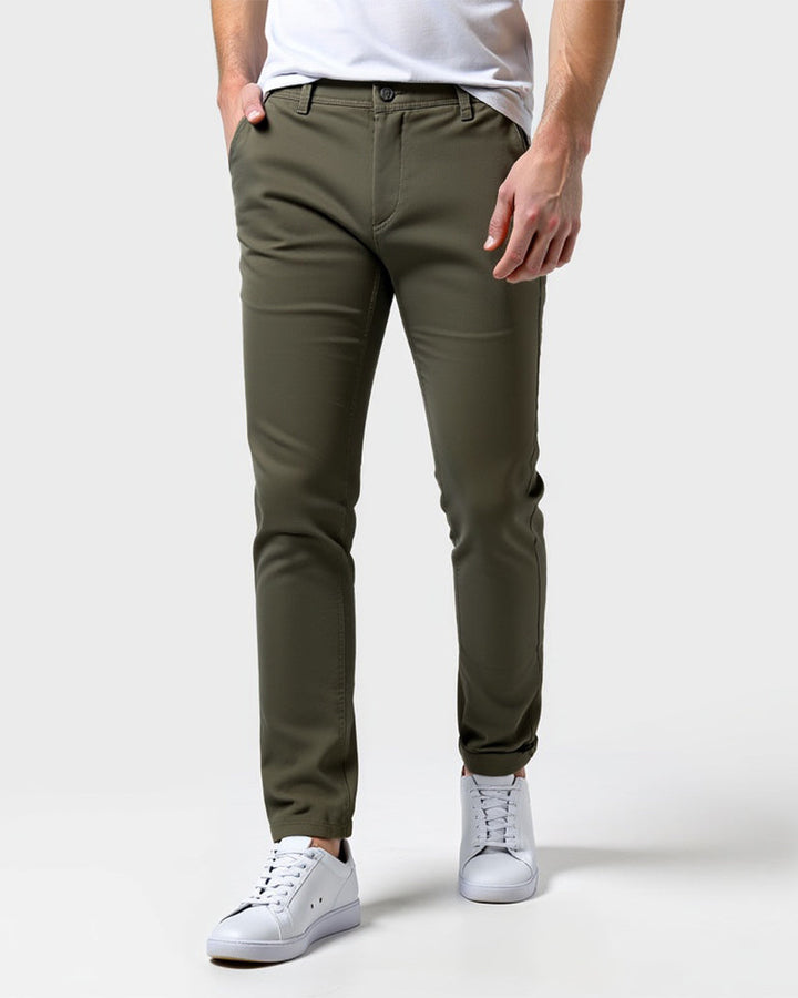 Front view of olive green slim chinos worn with a white tee and white sneakers, one hand in the front pocket. 13
