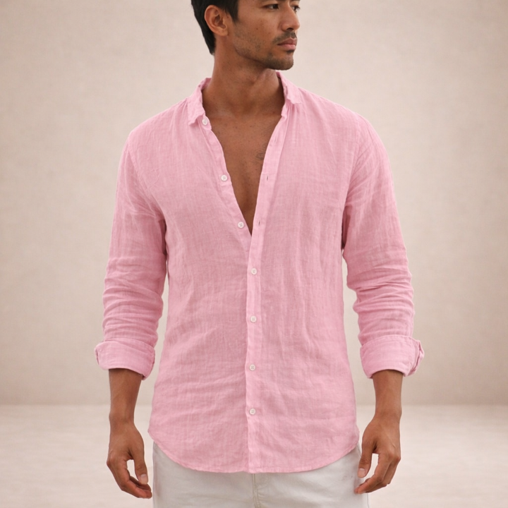 Model in a pink linen shirt with sleeves rolled and top buttons open, glancing sideways, paired with white pants.
