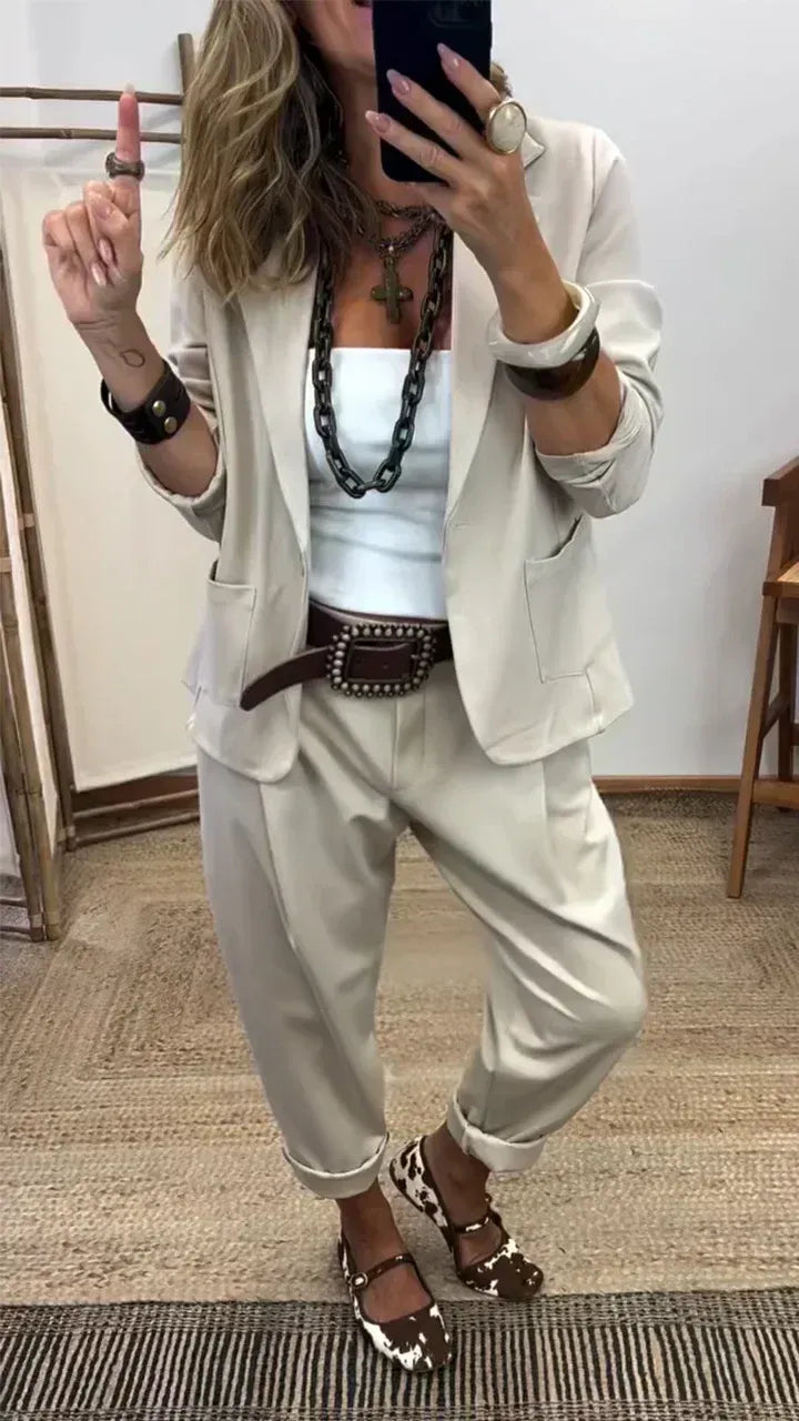 Light beige suit set with a blazer and cuffed pants, styled with a white top and brown studded belt.