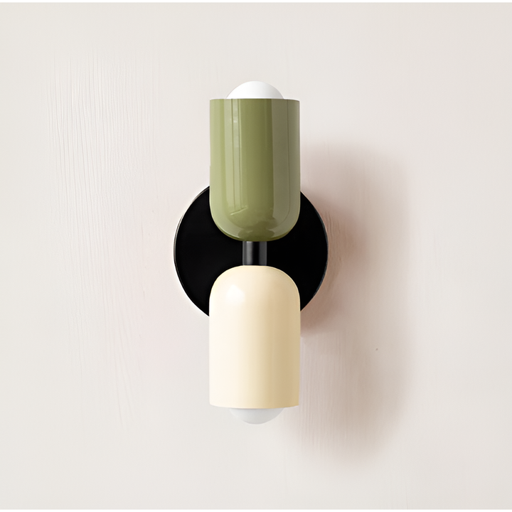 Wall light with a green upper head and cream lower head on a round black backplate, mounted on a pale wall. 21