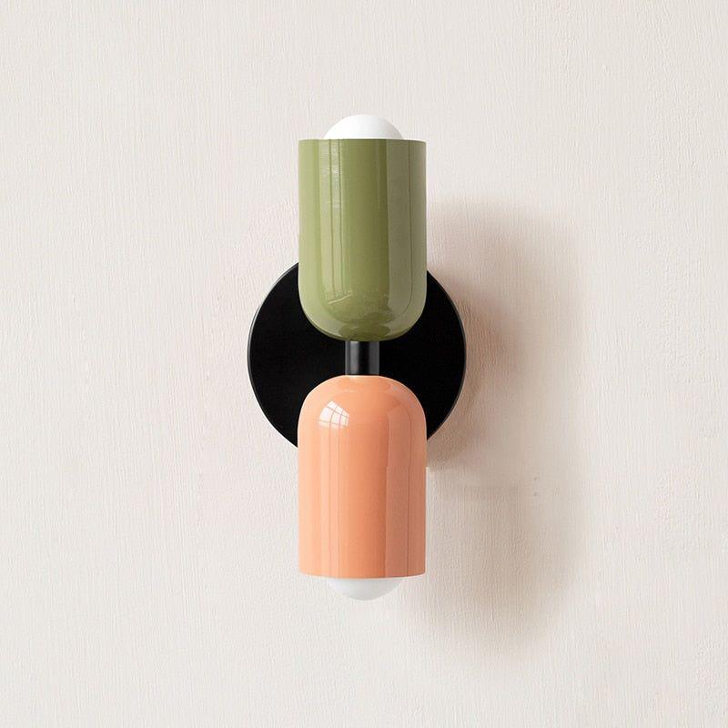 Wall light with a green upper head and peach lower head on a black round backplate. 13