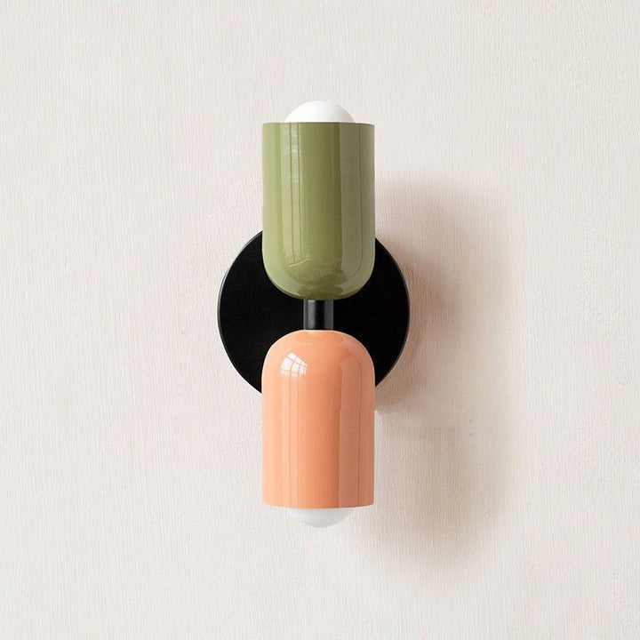 Wall light with a green upper head and peach lower head on a black round backplate. 13