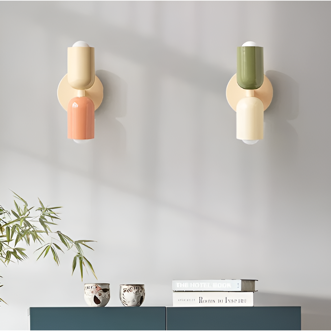 Two wall lights mounted on a gray wall above a teal cabinet, one cream and peach, one green and cream. 2