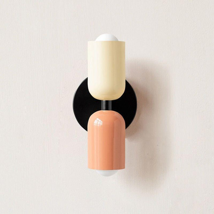 Wall light with a cream upper head and peach lower head on a black round backplate. 3