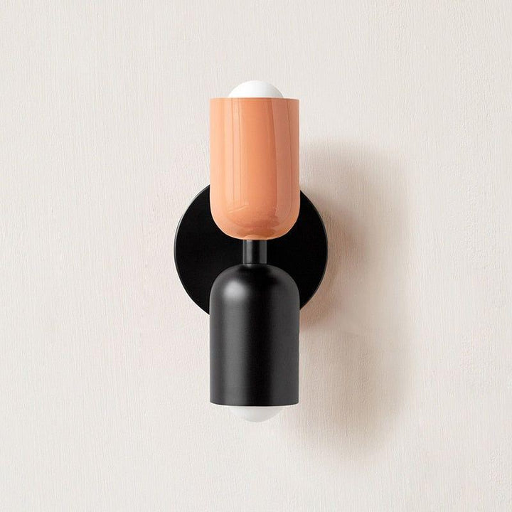 Wall light with a peach upper head and matte black lower head on a black round backplate. 5
