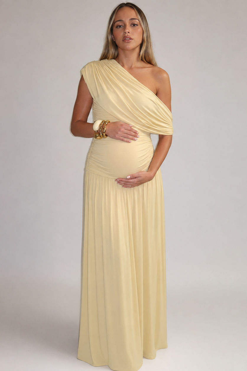 Front view of a yellow maternity maxi dress with an asymmetric neckline, draped sash and ruched bodice.