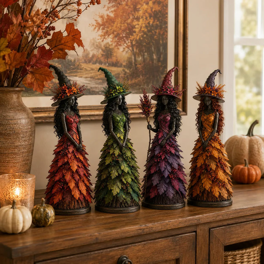 All four witch figurines lined up on a wooden sideboard with pumpkins, a glowing candle holder and a vase of autumn leaves. 7