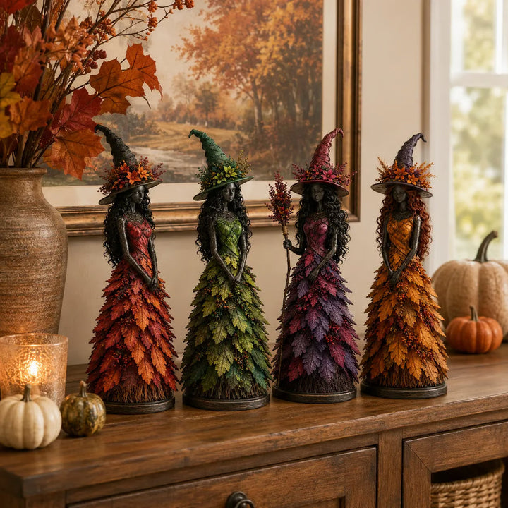 All four witch figurines lined up on a wooden sideboard with pumpkins, a glowing candle holder and a vase of autumn leaves. 7