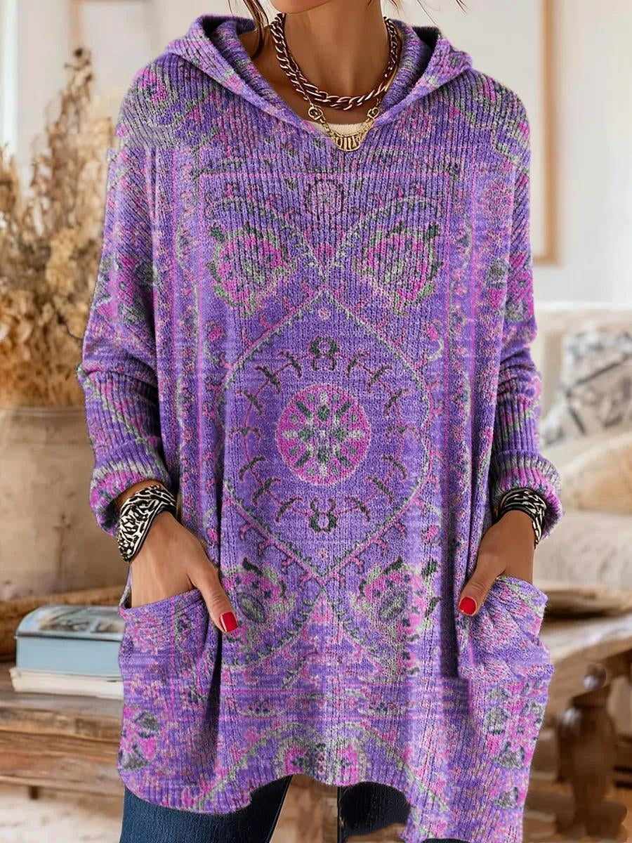 Model wearing the same hooded tunic in purple with pink and green medallion print, relaxed fit, hands tucked into front pockets. 2