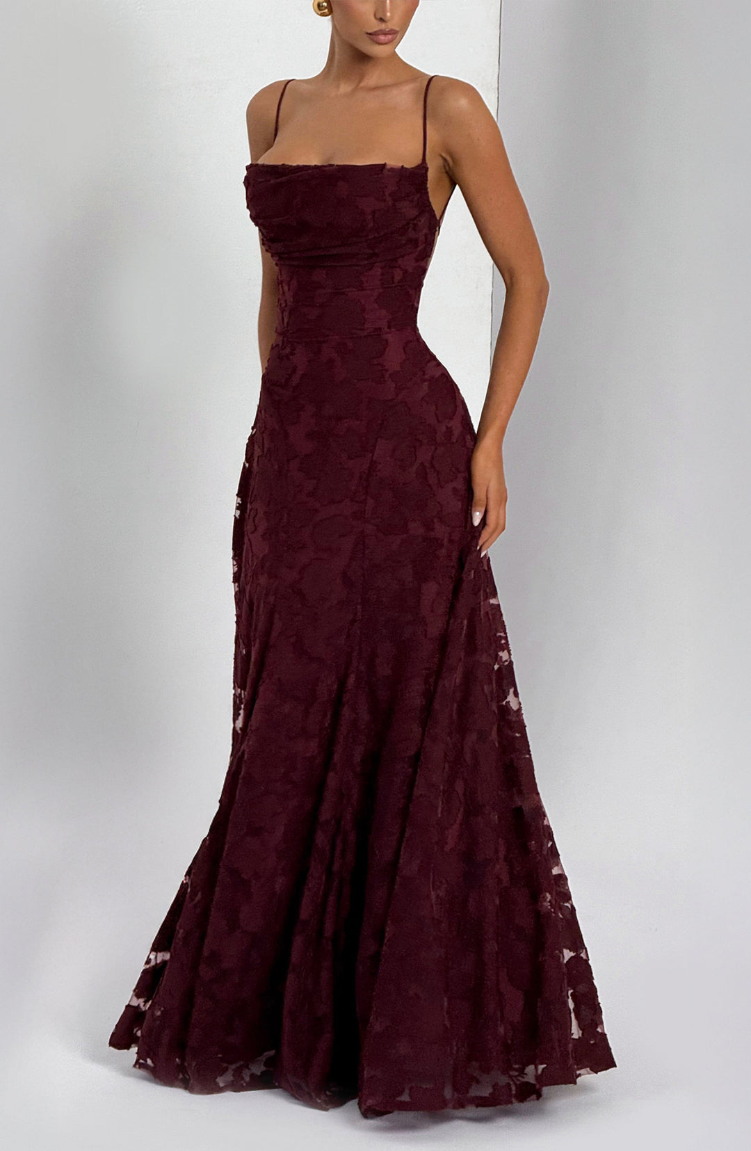 Burgundy floral textured gown with a flared skirt and ruched square neckline, styled at an angle against a pale wall. 22