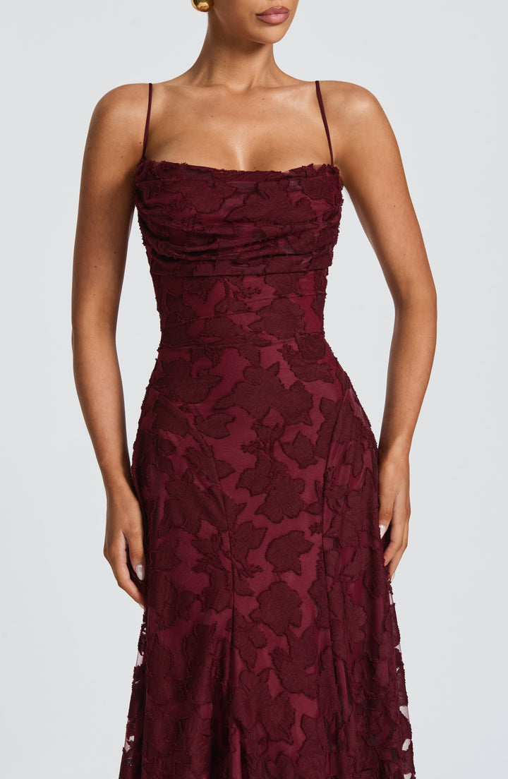 Close-up of a burgundy floral jacquard bodice with a ruched cowl neckline and thin spaghetti straps on a model. 21