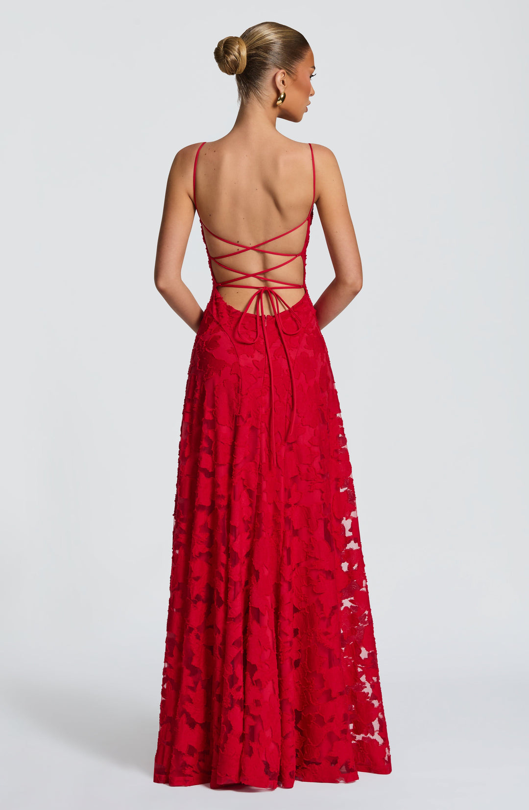 Back view of the red gown with criss-cross tie straps, an open back, a back zip and floral textured skirt. 27