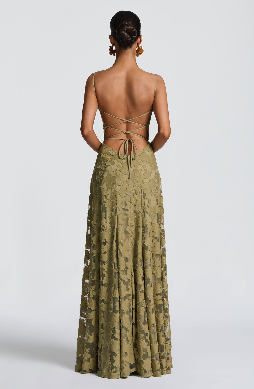 Back view of the olive green gown showing criss-cross lace-up straps, an open back, a center zip and sheer floral skirt. 34