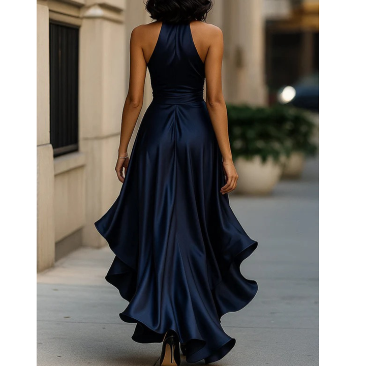 Women's navy satin dress, back view, showing the high halter neck, open shoulders and the flowing ruffled hem.