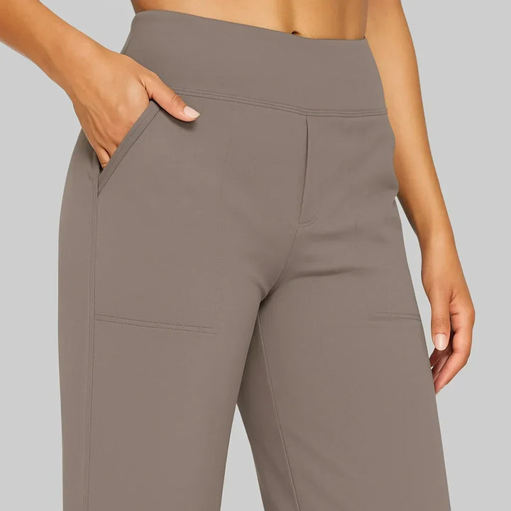 Women's taupe-brown pants detail of the wide waistband, slanted side pocket and stitched patch pocket, with a hand resting in the pocket.
