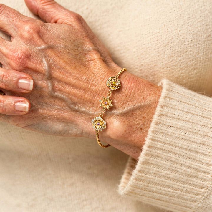 Older woman wearing the gold birth flower bracelet with a soft cream knit sleeve.