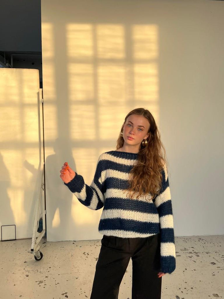 Frau in gestreiftem Pullover, blau-weiß, steht vor sonniger Wand, modisch, lässig, Herbstmode.