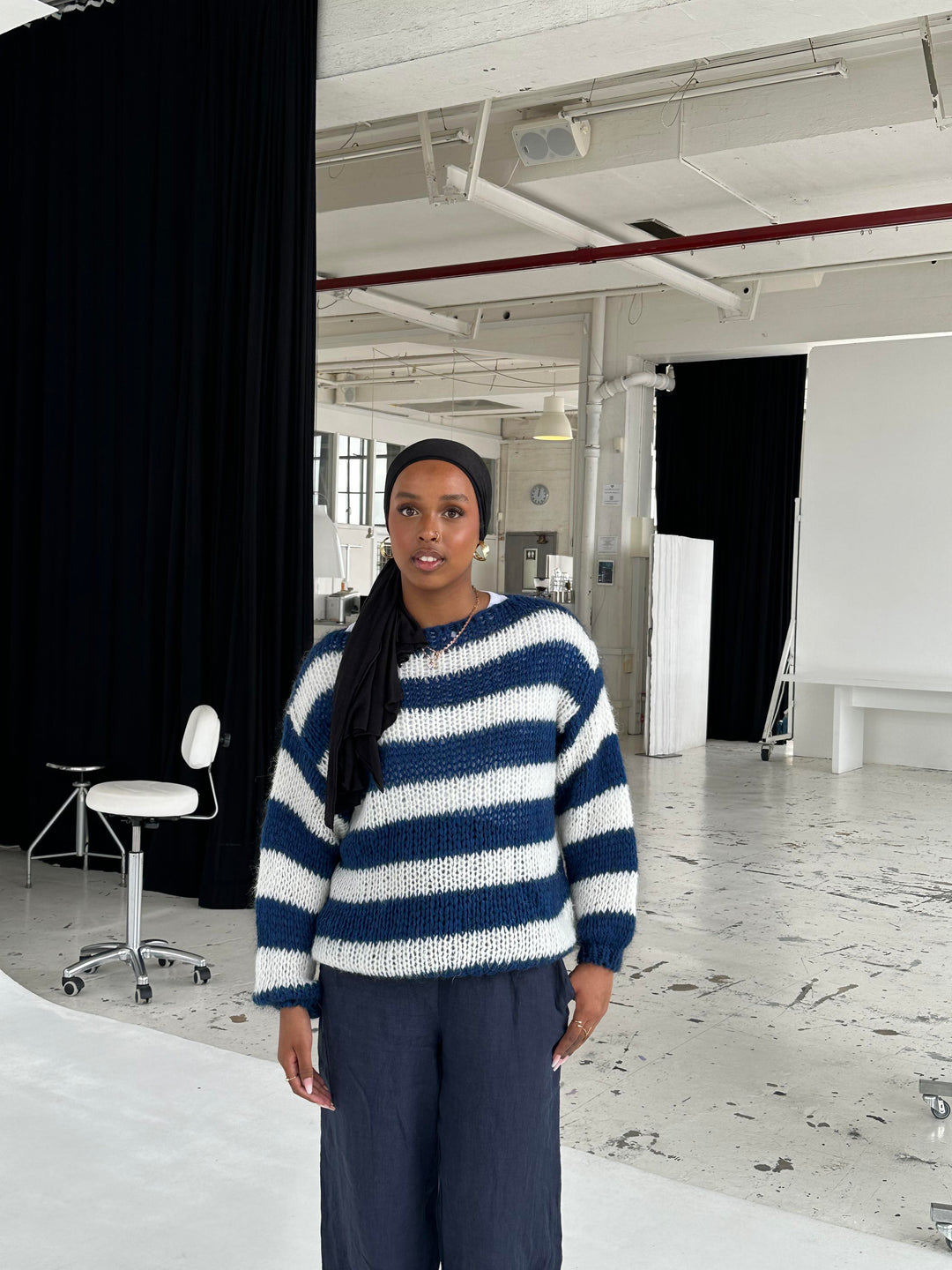 Frau in gestreiftem Pullover und dunkler Hose in modernem Fotostudio.