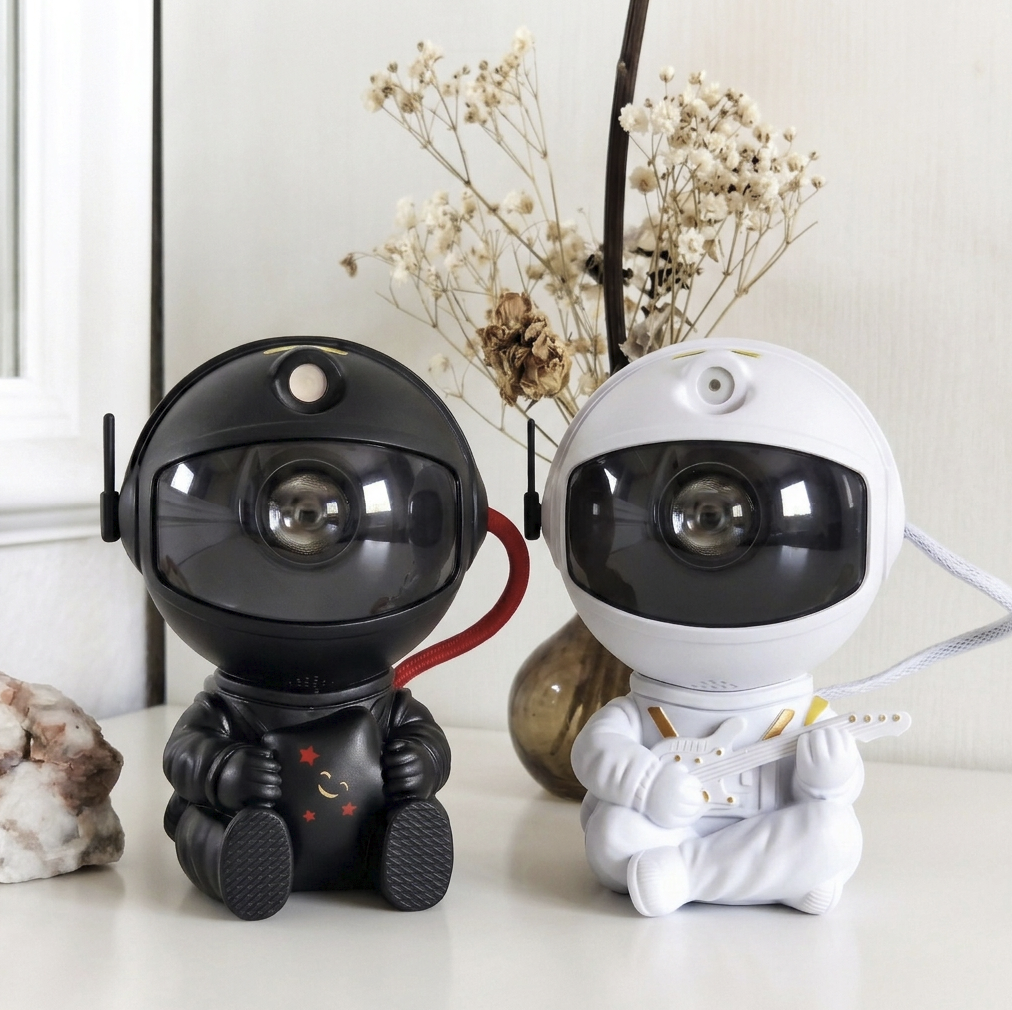 Black astronaut projector and a white guitar-playing version on a shelf with dried flowers and a mineral.