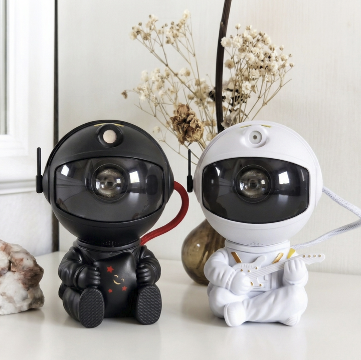 Black astronaut projector and a white guitar-playing version on a shelf with dried flowers and a mineral.