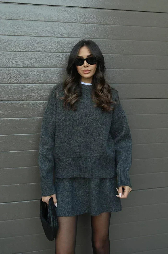 Charcoal gray knit sweater and flared skirt with sheer tights, sunglasses and a black woven clutch 11