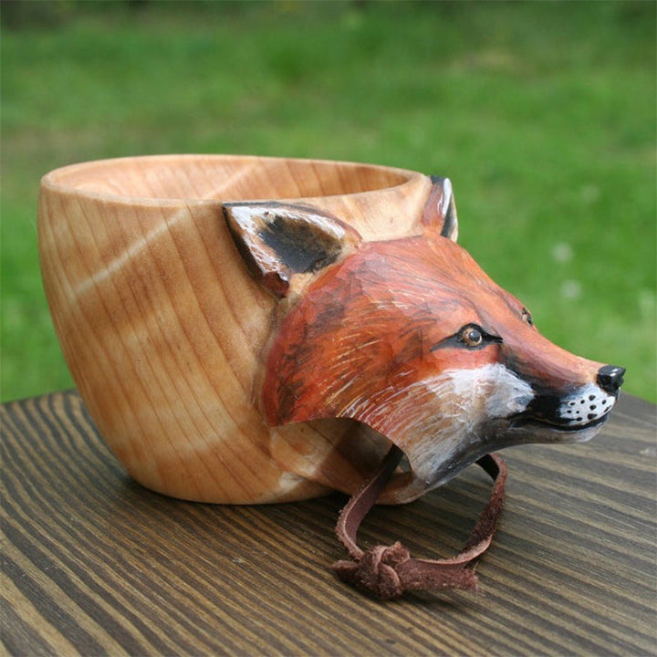 Handmade wooden cup detail with an orange fox head and a leather cord
