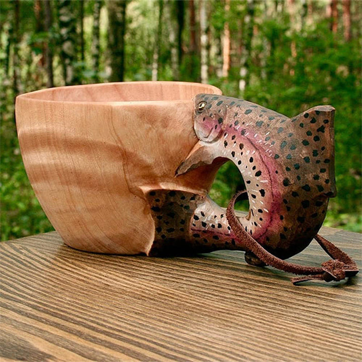 Handmade wooden cup detail with a carved trout handle and a leather cord