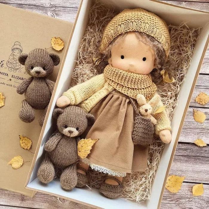 Doll in mustard knit hat, scarf and cardigan with brown dress, boxed with two knit teddy bears among autumn leaves 6