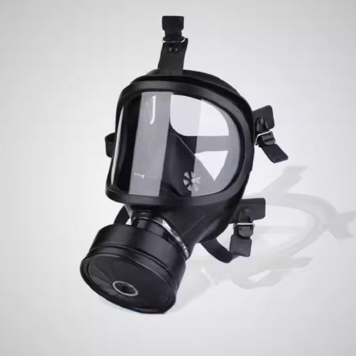 Black NBCR protective mask with a clear visor and round filter canister on a gray background.