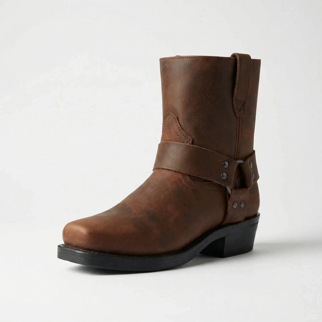 Brown leather harness boot in three-quarter view with a square toe, studded ankle strap, pull tab and stacked black heel. 4