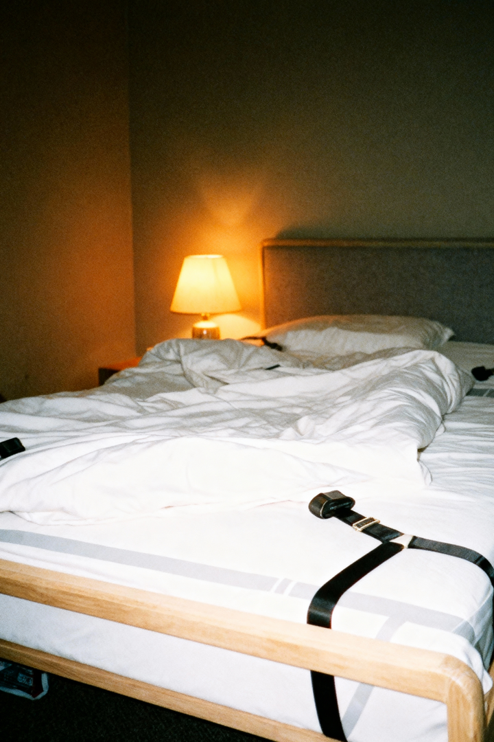 Detail of a black restraint strap and cuff on rumpled white bedding