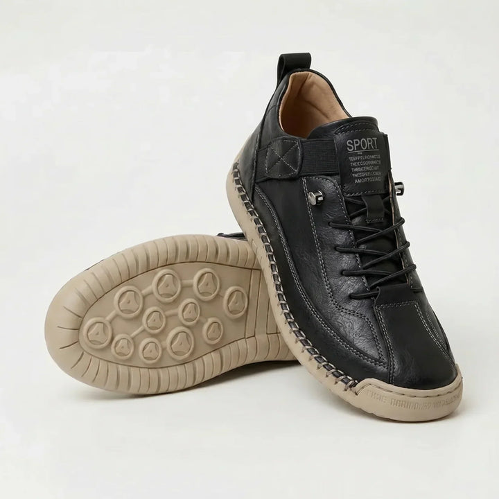 Black textured sneakers with a beige stitched sole, one shoe upright and one turned to show the dotted tread 12