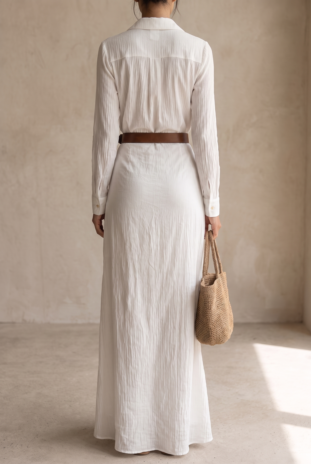 Back view of the yellow maxi dress showing the yoke pleat, cuff buttons and brown belt, with a tote in one hand.