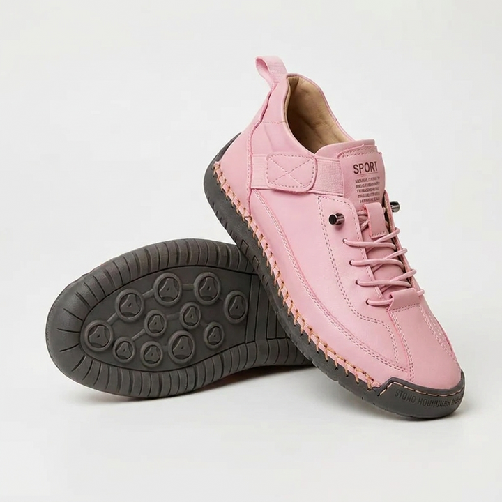 Pink sneakers with a dark gray stitched sole, one shoe standing and one flipped to show the tread 14