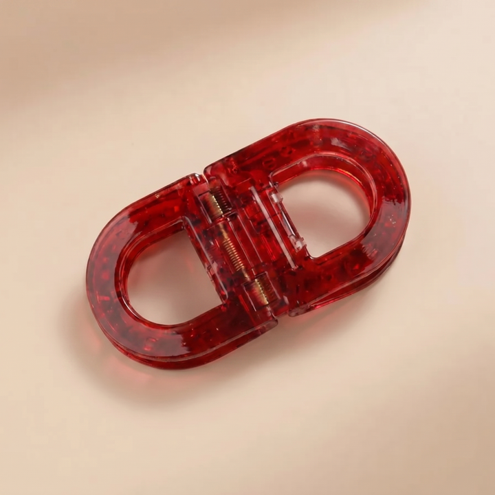 Flat Grip Magnetic Hair Clip in translucent ruby red with a gold spring, shown on a beige background.