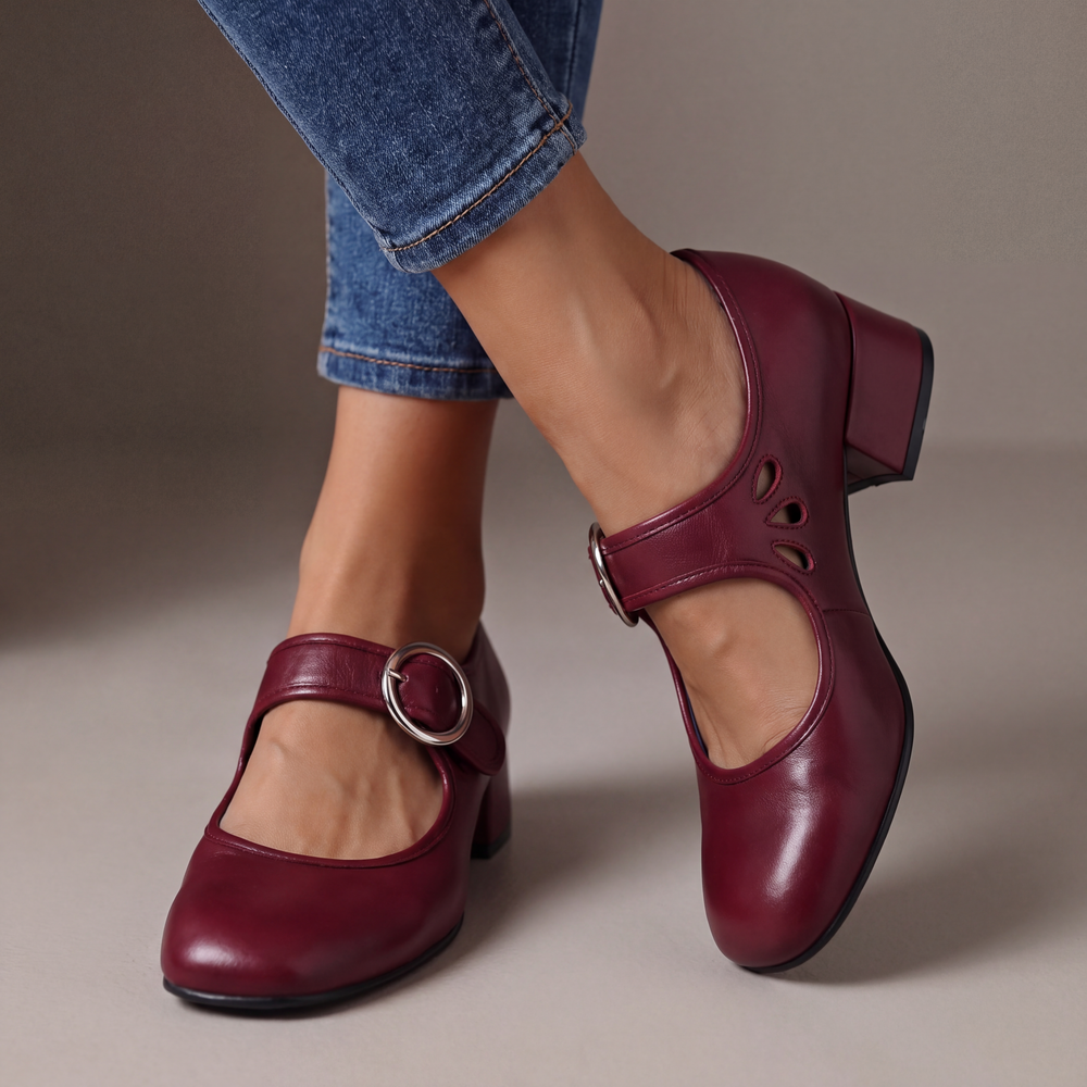 Burgundy red leather block-heel pumps with a round silver buckle strap and teardrop cutouts, worn with cuffed blue jeans. 2