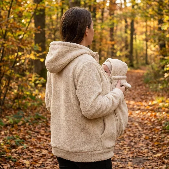 Back view of a woman in a cream fleece hoodie carrying a baby in the front pouch.
