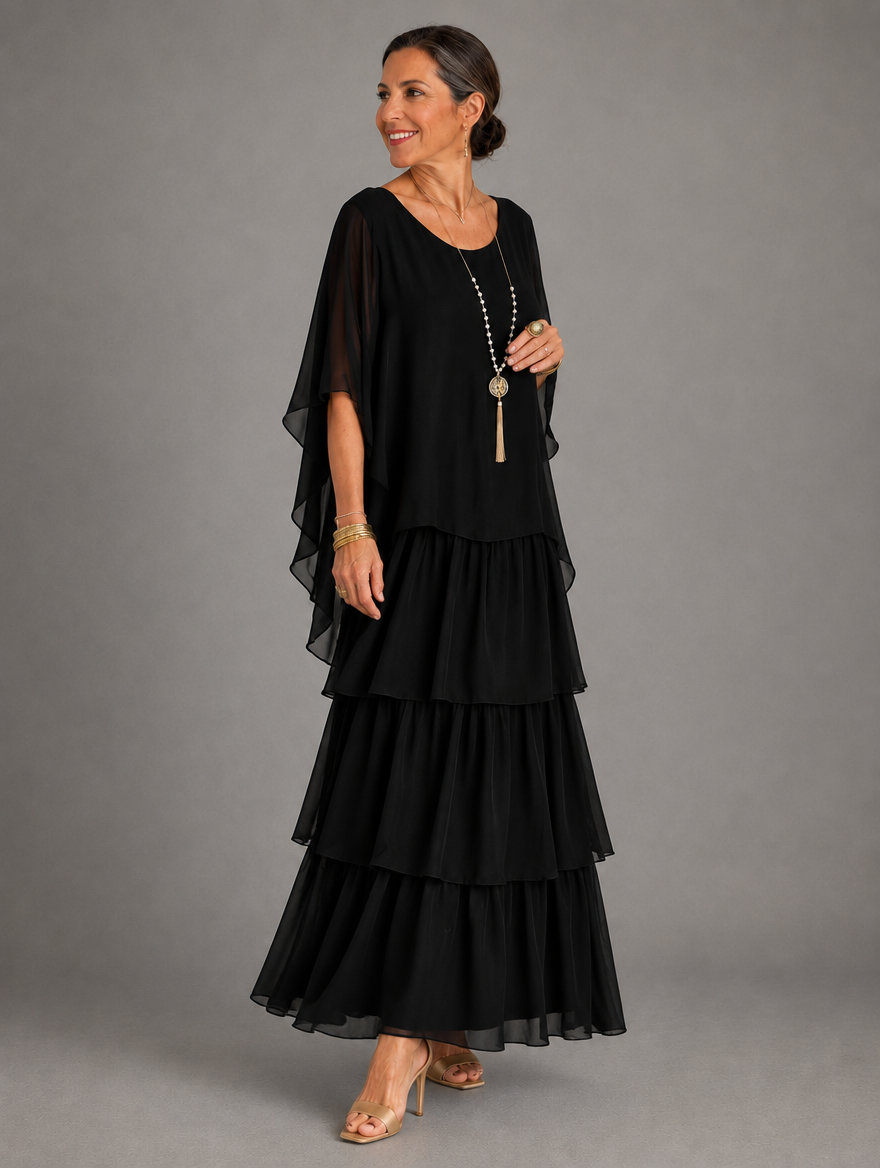 Side view of the black tiered chiffon maxi dress with a draped cape sleeve and layered ruffled skirt, worn with gold heels